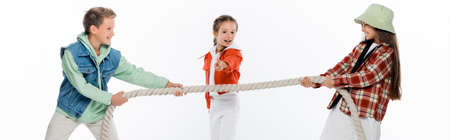 preteen kid looking at friends pulling rope while playing tug of war game isolated on white, bannerの写真素材