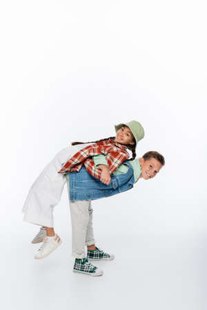 full length of happy boy piggybacking cheerful girl in panama hat on whiteの写真素材