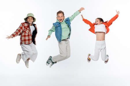 full length of stylish kids smiling while levitating on whiteの写真素材