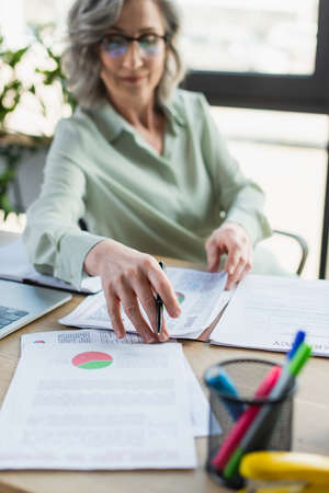 Documents and laptop near blurred businesswoman working in officeの写真素材