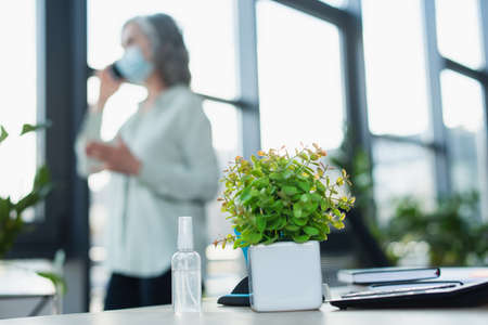 Hand sanitizer near plant and blurred businesswoman in officeの写真素材