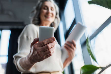 Low angle view of blurred businesswoman holding smartphone and blueprint in officeの写真素材