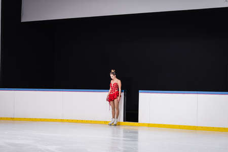 full length of young worried figure skater in red dress standing on ice rinkの写真素材