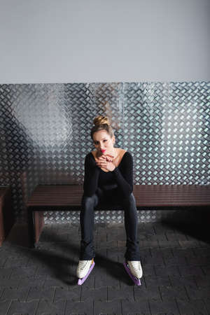 full length of pleased woman in white figure skates and black bodysuit sitting on bench
