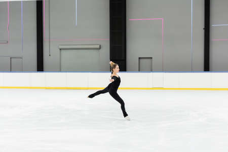full length of professional figure skater in bodysuit skating with outstretched hands in ice arenaの写真素材