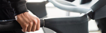 Cropped view of man training on blurred treadmill in gym, banner