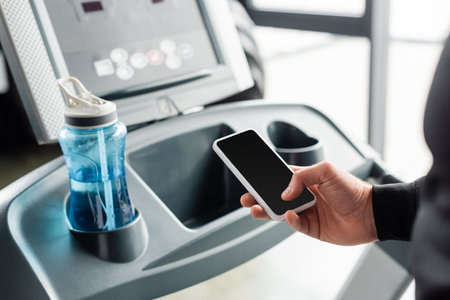 Cropped view of sportsman using cellphone on treadmill in sports centerの写真素材
