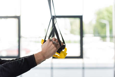 Cropped view of sportsman pulling suspension straps in sports center