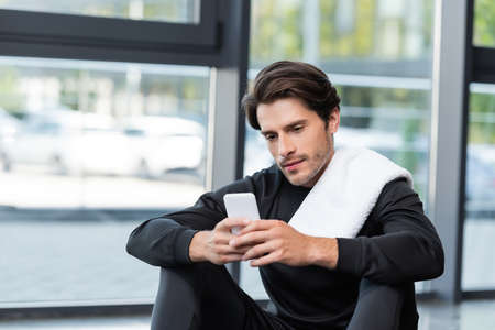 Brunette sportsman with towel using mobile phone in sports center