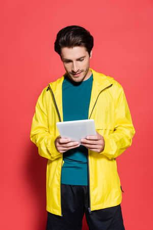Sportsman in yellow sports jacket using digital tablet on red background