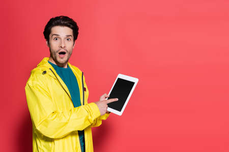 Excited sportsman pointing at digital tablet with blank screen on red background