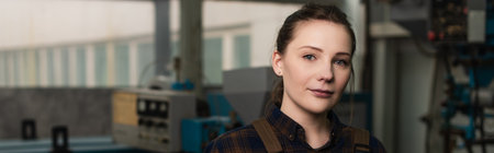 Young welder looking at camera in blurred factory, bannerの写真素材