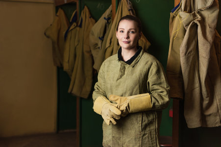 Welder in gloves and uniform looking at camera in dressing room of factoryの写真素材