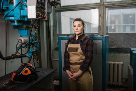 Welder in overalls standing near welding machine and protective mask in factory