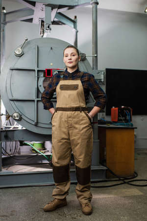 Young welder in overalls looking at camera near vacuum laser welding machine in factory