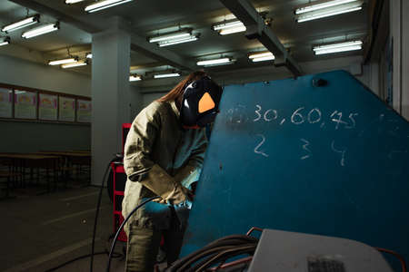 Welder in protective helmet working in factoryの写真素材