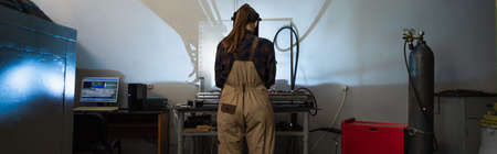 Back view of welder in overalls working near gas cylinder in factory, banner