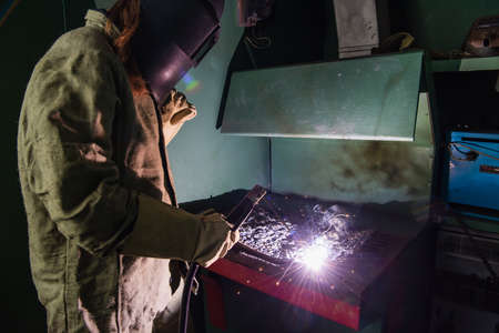 Welder in mask with visor working with welding torch in factory