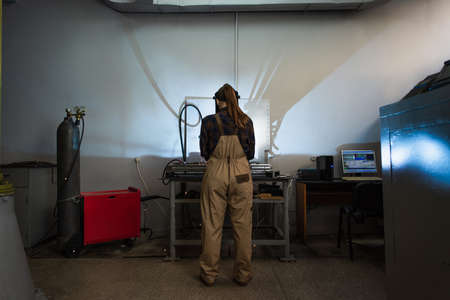 Back view of brunette welder working near gas cylinder and computer in factory