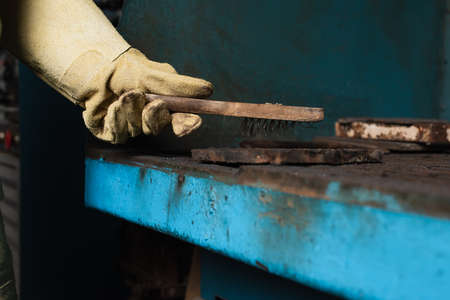Cropped view of welder in protective glove holding brush above detail in factoryの写真素材
