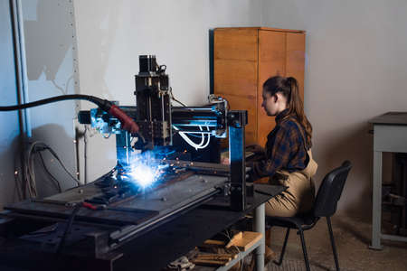 Side view of welder sitting near keyboard and welding machine in factory