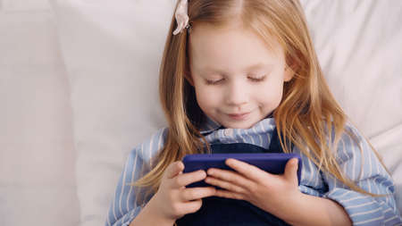 Smiling child holding mobile phone in bedroom