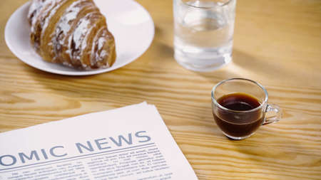 glass cup of espresso near newspaper, water and croissant,stock image
