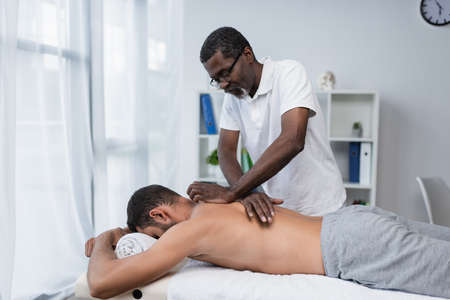 mature african american rehabilitologist doing back massage to young manの写真素材