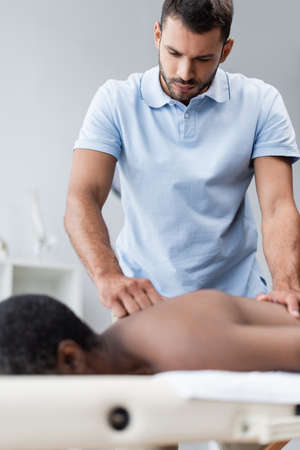 young chiropractor doing back massage while treating blurred african american manの写真素材