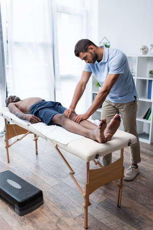 full length view of mature african american man lying on massage table during massotherapyの写真素材