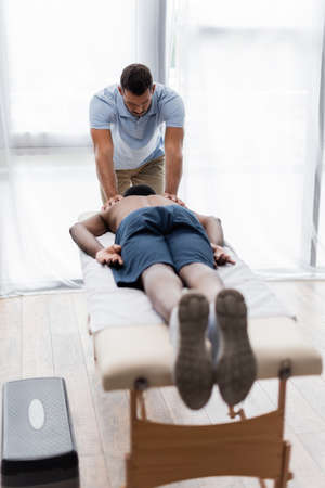young physiotherapist treating african american man lying on massage table