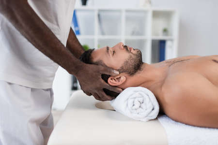 side view of young man getting treating massage by african american rehabilitologistの写真素材