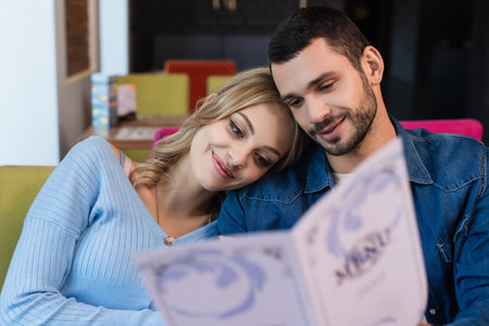 happy couple sitting head to head while choosing meal from blurred menuの写真素材