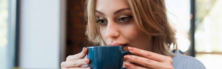 young blonde woman drinking coffee in restaurant, banner
