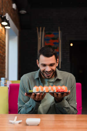 amazed man holding plate with set of delicious sushi rolls in restaurantの写真素材