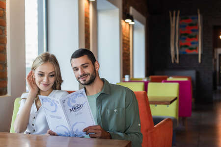 smiling couple choosing meal from menu while sitting in restaurantの写真素材
