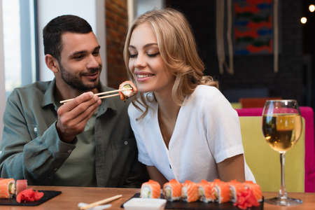 young man feeding happy woman with sushi roll during dinner in restaurantの写真素材