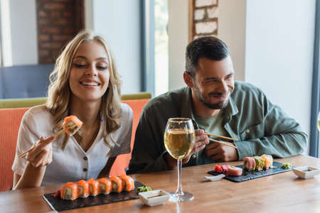 cheerful man with closed eyes eating sushi near smiling girlfriend in restaurantの写真素材
