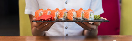 partial view of woman holding plate with tasty sushi rolls, bannerの写真素材