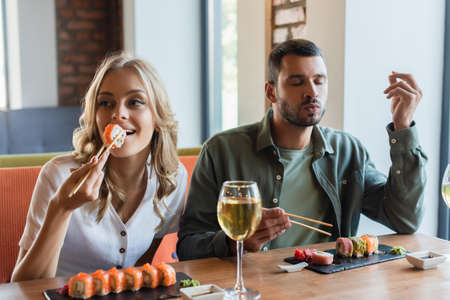 man with closed eyes enjoying delicious sushi near smiling girlfriendの写真素材