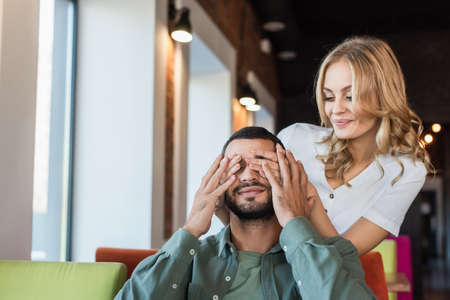 smiling woman covering eyes of boyfriend with hands while playing guess who gameの写真素材