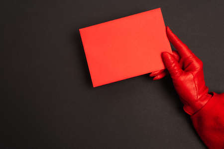 cropped view of person in red glove holding envelope on blackの写真素材