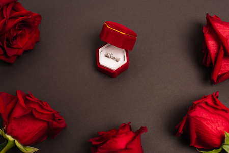 top view of jewelry box with diamond ring near red roses on blackの写真素材