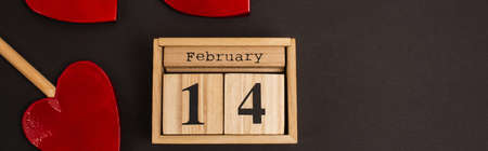 top view of wooden calendar with 14 february lettering near heart-shaped lollipops on black, bannerの写真素材