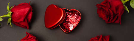 top view of metallic box with red confetti hearts near roses on black, bannerの写真素材