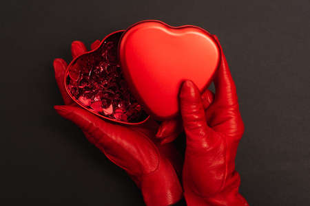 top view of woman in red gloves holding metallic heart-shaped box on black