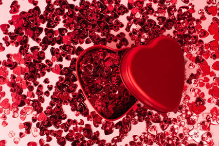 top view of metallic heart-shaped box near shiny red confetti hearts on pinkの写真素材