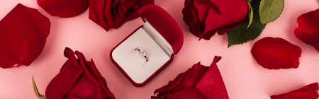 flat lay of red rose petals around jewelry box with diamond ring on pink, bannerの写真素材