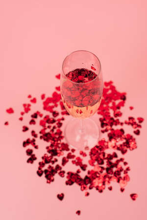 high angle view of glass with champagne and red heart-shaped confetti on pinkの写真素材