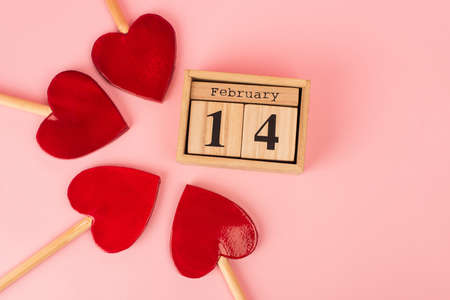 flat lay of heart-shaped lollipops near wooden calendar with 14 february on pinkの写真素材